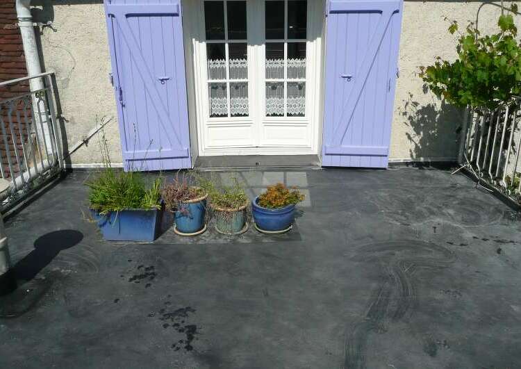 toit terrasse couvert en membrane EPDM, au fond un mur avec la porte fenêtre au volets bleus, de chaque coté des garde-corps, au milieu quatre plantes en pots.