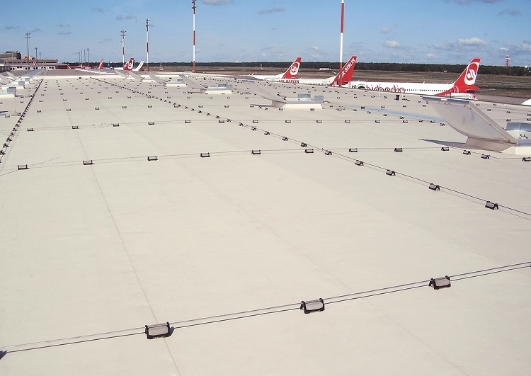 grande surface de toiture plate couverte en membrane TPO, à l'arrière plan des avions de grandes lignes et les pistes de l'aéroport.